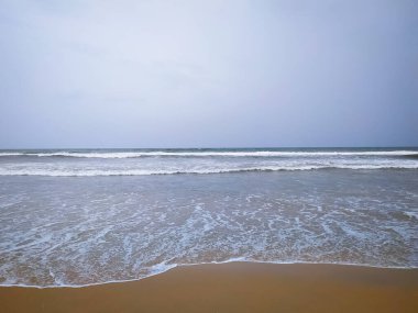 Bulutlu bir günde kumlu bir sahilde bulanık bir arka planda deniz dalgaları.