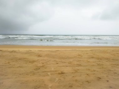 Kum sahilinde bulutlu arka planda dalgalar