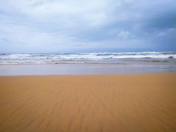 Soft white ocean wave on clean sandy beach with cloudy sky