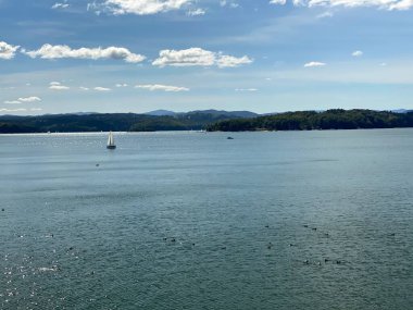 Solinie Gölü üzerinde hafif bulutlu bir hava var Bieszczady Dağları 'nın tepeleri kozalaklı ormanlarla kaplı.