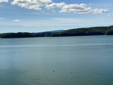Solinie Gölü üzerinde hafif bulutlu bir hava var Bieszczady Dağları 'nın tepeleri kozalaklı ormanlarla kaplı.