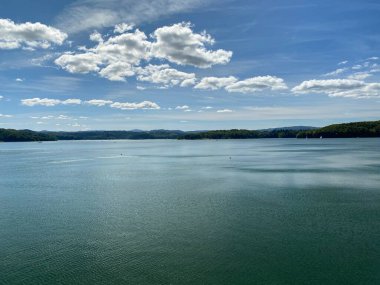 Solinie Gölü üzerinde hafif bulutlu bir hava var Bieszczady Dağları 'nın tepeleri kozalaklı ormanlarla kaplı.