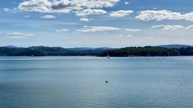Solinie Gölü üzerinde hafif bulutlu bir hava var Bieszczady Dağları 'nın tepeleri kozalaklı ormanlarla kaplı.