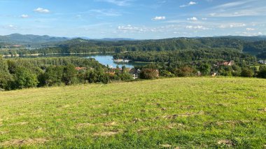 Solinie Gölü üzerinde hafif bulutlu bir hava var Bieszczady Dağları 'nın tepeleri kozalaklı ormanlarla kaplı.