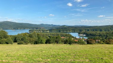Solinie Gölü üzerinde hafif bulutlu bir hava var Bieszczady Dağları 'nın tepeleri kozalaklı ormanlarla kaplı.