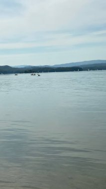 Solinie Gölü üzerinde hafif bulutlu bir hava var Bieszczady Dağları 'nın tepeleri kozalaklı ormanlarla kaplı.