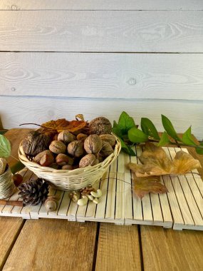 ceviz ve fındıklar bir sepetin içinde, meşe ağacından yapılmış paletlerin üzerinde, arka planda görünen saman yapraklarının üzerinde, çam ağacından beyaza boyanmış.