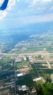 blue sky swirling clouds roads forests and fields on ground view of wing of aircraft
