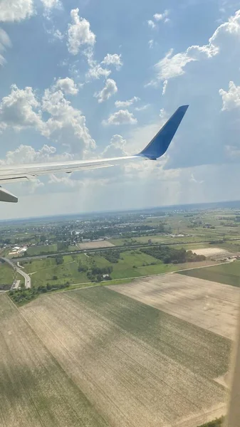 blue sky swirling clouds roads forests and fields on ground view of wing of aircraft