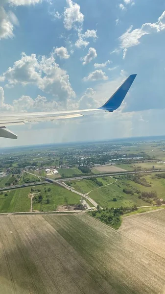 blue sky swirling clouds roads forests and fields on ground view of wing of aircraft