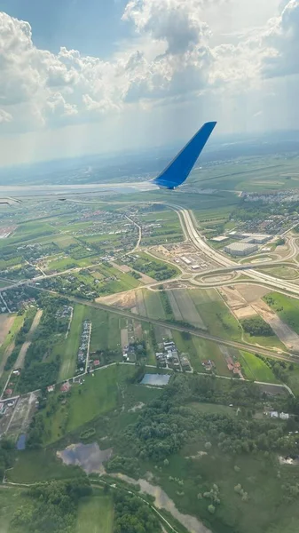 blue sky swirling clouds roads forests and fields on ground view of wing of aircraft