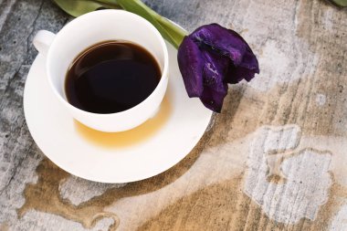 Beyaz bir fincanla mor bir lalenin yanındaki ahşap masaya kahve dökülmüş. .