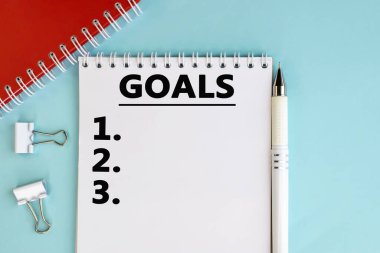 Hedefin sözcüğü, kırtasiyenin yanındaki mavi arkaplanda duran açık bir deftere yazılmıştır..