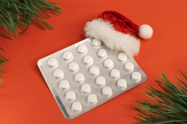 İçinde haplar ve ladin dalları arasında kırmızı arka planda bir Noel Baba şapkası olan kabarcık. Tıbbi konsept ve Noel