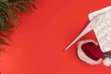 Noel arkaplanı. Kırmızı arka planda yeni yıl şapkası ve ladin olan tıbbi malzemeler. Metin için yer