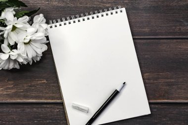 Ahşap bir masada bir buket kasımpatı içeren boş bir defter aç..