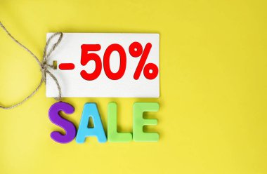 50 percent discount price tag on yellow background. The word sale made from colored plastic letters.