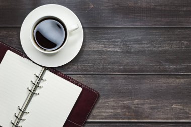 Açık bir defter ve bir fincan kahve. Tahta, koyu bir masada. Metin için yer.