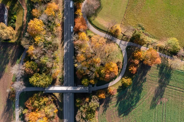 Vista de cima para baixo em uma paisagem outonal com uma rua rural e uma ponte coberta para pedestres diretamente de cima em Oberhaching. — Fotografia de Stock