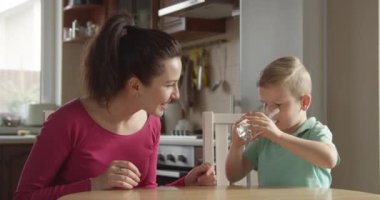 KId, bir bardak su içiyor. Annem de mutfağın yanında oturuyor.