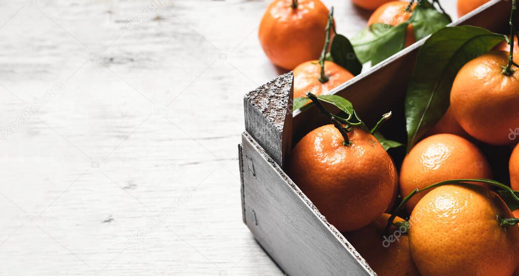 A box with fresh tangerines on on a white wooden table with copy space