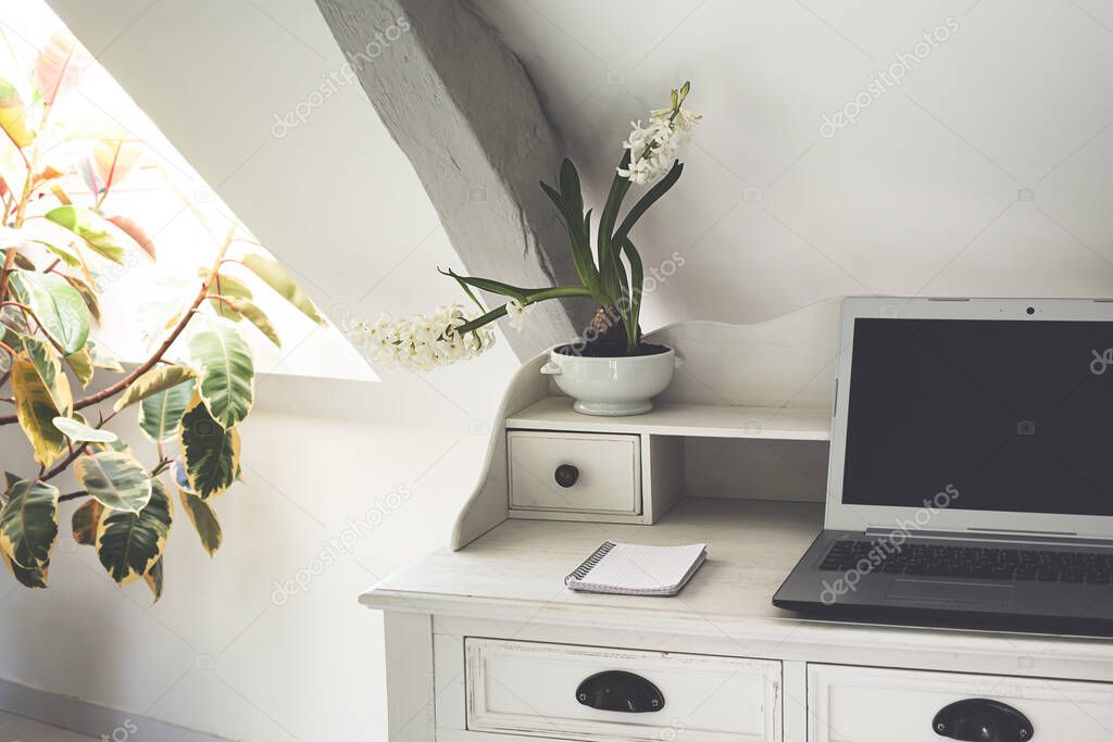 A white table with a laptop near the window in the room with home plants, the concept of work from home, remote work, freelance, work during quarantine