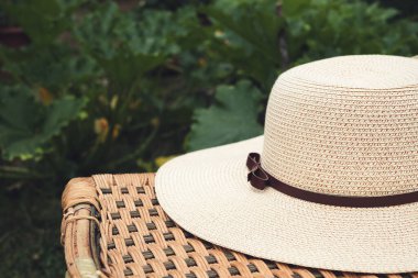 Women's summer hat on an old wicker chair in a garden close-up, sustainability and gardening concept