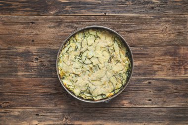 Zucchini pie, baked with parmesan, eggs and herbs in baking dish on the wooden background, top view with copy space