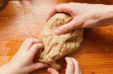 Kadın ve çocuğun eli ahşap masada kurabiye için hamur yoğuruyor.