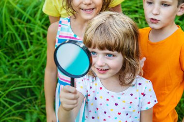 Çocuklar doğadaki büyütece bakarlar. Seçici odaklanma. Doğa.