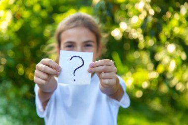 Çocuk üzerinde soru işareti olan bir kağıt tutuyor. Seçici odaklanma. Çocuk.