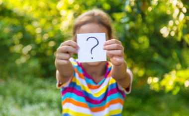 Çocuk üzerinde soru işareti olan bir kağıt tutuyor. Seçici odaklanma. Çocuk.