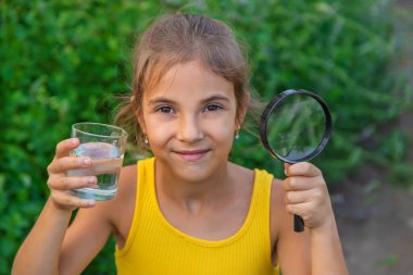 Çocuk bir bardak suyu bir büyüteçle inceliyor. Seçici odaklanma. Çocuk.