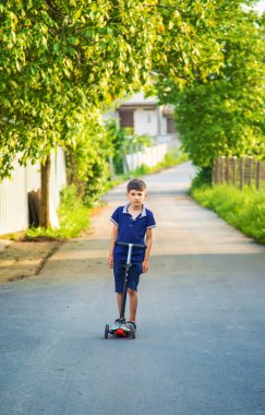 Çocuk sokağın aşağısında bir scooter kullanıyor. Seçici odaklanma. Çocuk.