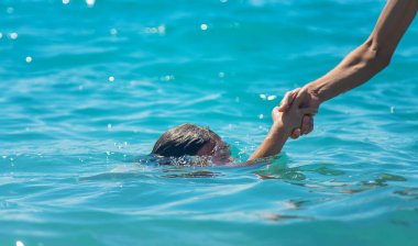 The child is drowning in the water the hand of salvation. Selective focus. People.