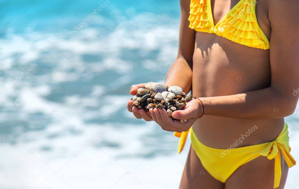 A child on the beach holds sea stones in her hands. Selective focus. Kid.
