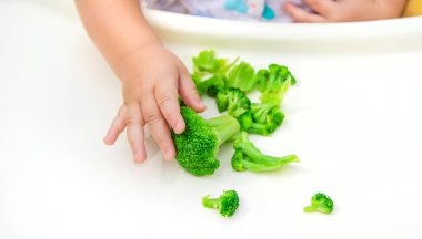 Bebek bir parça brokoli sebzesi yiyor. Seçici odak.