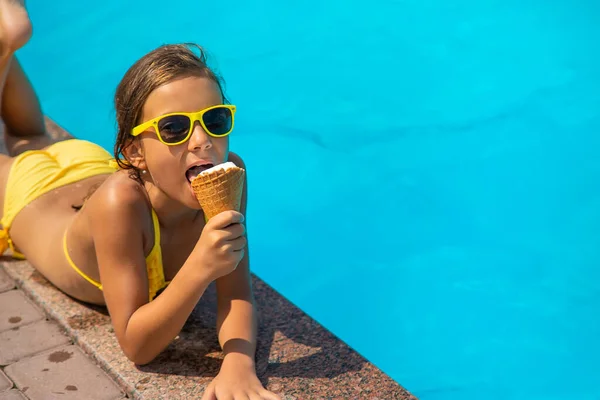 L'enfant mange de la glace près de la piscine. Concentration sélective. — Photo