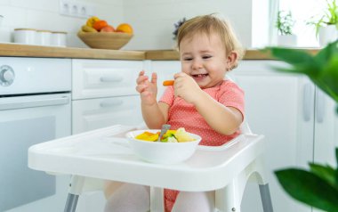 Bebek sandalyede sebze yiyor. Seçici odak.