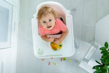 Bebek sandalyede sebze yiyor. Seçici odak.