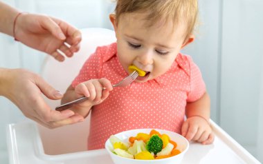 Bebek sandalyede sebze yiyor. Seçici odak.