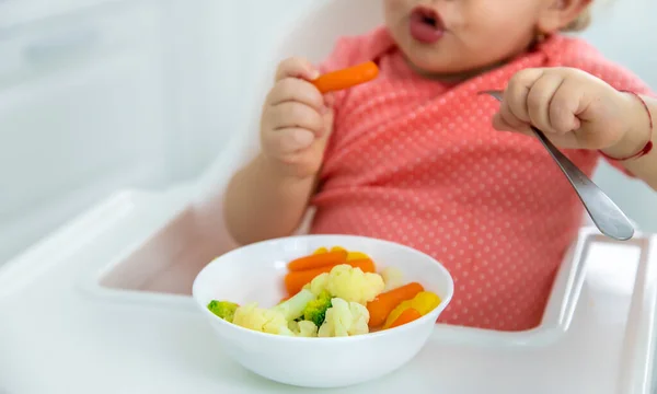De baby eet groenten op een stoel. Selectieve focus. — Stockfoto