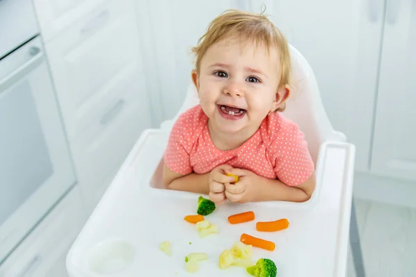 O bebê come legumes em uma cadeira. Foco seletivo. — Fotografia de Stock