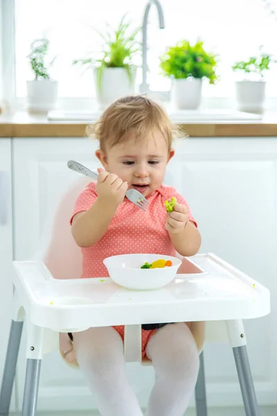 O bebê come legumes em uma cadeira. Foco seletivo. — Fotografia de Stock