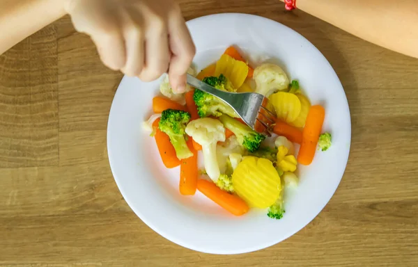 A criança come verduras em uma cadeira. Foco seletivo. — Fotografia de Stock