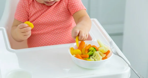 O bebê come legumes em uma cadeira. Foco seletivo. — Fotografia de Stock