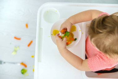 Bebek sandalyede sebze yiyor. Seçici odak.