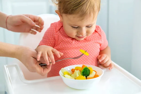 The baby eats vegetables on a chair. Selective focus. — Stock Photo, Image