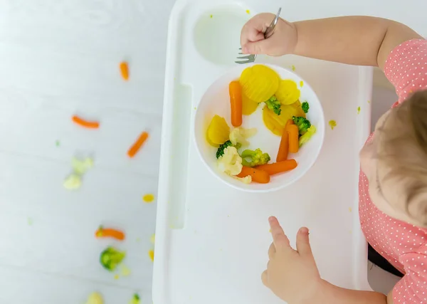 O bebê come legumes em uma cadeira. Foco seletivo. — Fotografia de Stock