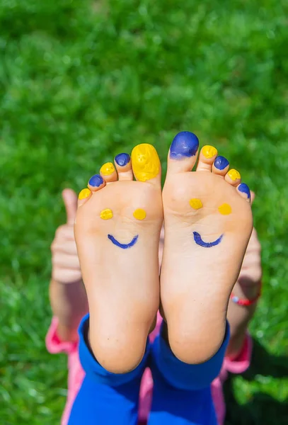 Child feet on the grass Ukrainian flag. Selective focus. — Foto Stock